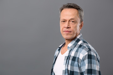 Male portrait. Serious nice man looking at you while standing against grey background