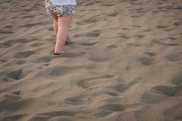 Baby girl is running on sand, view on her legs.