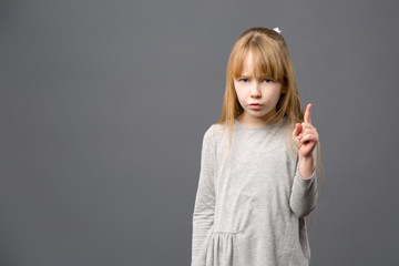 Intelligent child. Smart blonde girl pointing up with her finger while talking to you