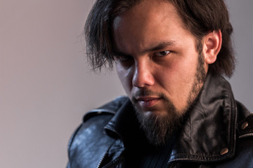 Fototapeta premium Terrible look of the guy with a beard in a black leather jacket. Portrait of a Man in a rock or a biker style.