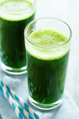 Healthy green smoothie made from spinach, apple and cucumber in a jars with red straw on white wooden table