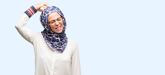 Middle age muslim arab woman wearing hijab doubt expression, confuse and wonder concept, uncertain future isolated blue background