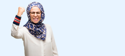 Middle age muslim arab woman wearing hijab irritated and angry expressing negative emotion, annoyed with someone isolated blue background
