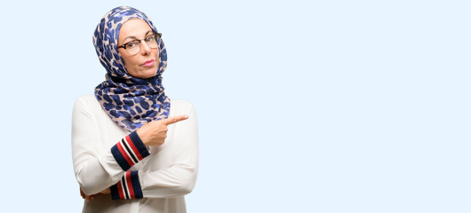 Middle age muslim arab woman wearing hijab pointing away side with finger isolated blue background