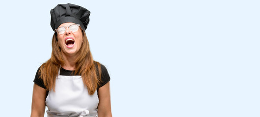 Middle age cook woman wearing chef apron stressful, terrified in panic, shouting exasperated and frustrated. Unpleasant gesture. Annoying work drives me crazy isolated blue background