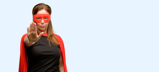 Middle age super hero woman wearing red mask and cape annoyed with bad attitude making stop sign...