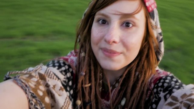 Portrait of young redhead woman taking selfie on the green fieldsin sunny day and spining around, portrait of happy hipster girl with dreadlocks
