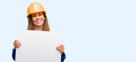 Engineer construction worker woman holding blank advertising banner, good poster for ad, offer or announcement, big paper billboard isolated blue background
