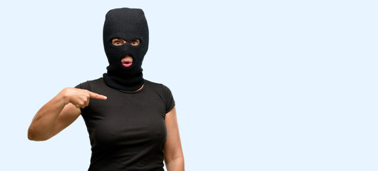 Burglar terrorist woman wearing balaclava ski mask happy and surprised cheering expressing wow gesture, pointing with finger isolated blue background