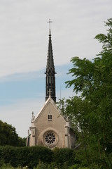 The top part of the catholic cathedral with spire, round window, cross in Meudon, Paris suburb among green trees in the sunny summer day