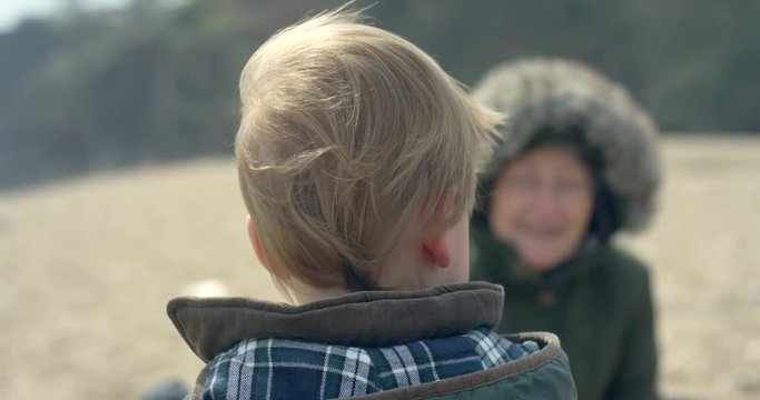 A little boy is on the beach and is looking at his grandmother