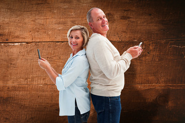 Happy mature couple using their smartphones against overhead of wooden planks