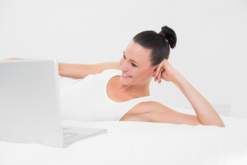 Obraz premium Casual smiling woman looking at laptop in bed