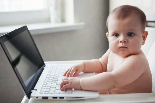 Baby sits on a white highchair with a laptop