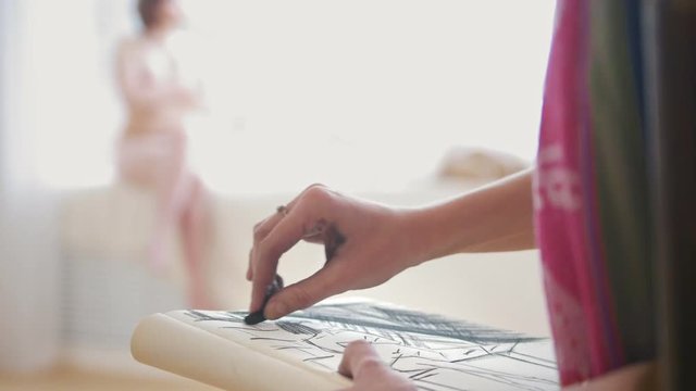 Female hands sketching naked model in light studio