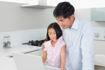 Smiling father and daughter using laptop in kitchen