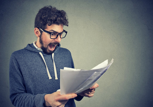 Angry stressed screaming man looking at documents papers