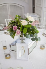 Table setting with a white tablecloth, beautiful flowers in vases, candlesticks. A tablet on the table for guests is three
