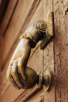 Golden doorknocker with hand shape on old wooden door