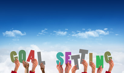 Hands holding up goal settings against bright blue sky over clouds
