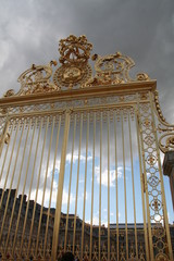 Golden main entrance royal gate to the Versailles palace in the grey and blue sky