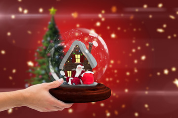 Composite image of hand holding snow globe against blurred christmas tree background