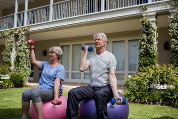 Senior couple exercising with dumbbells on fitness ball