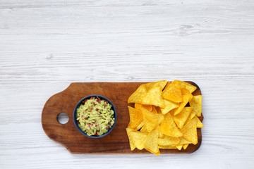 Full bowl of avocado dip guacamole with nachos on wooden board. Top view.