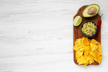 Bowl of traditional mexican guacamole and ingredients with nachos on wooden board. White wooden background. Top view. Copy space.