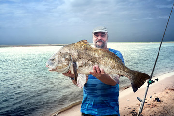 A fisherman is holding a huge fish  black drum (Pogonias cromis)  against the sea. Texas, the Mexican Gulf, the United States,