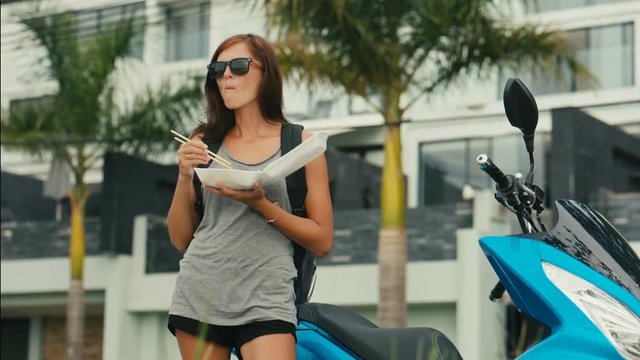 Woman Biker Eating Asian wok Noodle from Take away Box using chopsticks