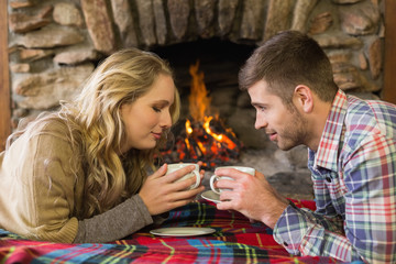 Couple with tea cups in front of lit fireplace