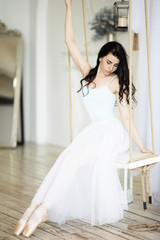 Young pretty ballerina is sitting on swing in studio