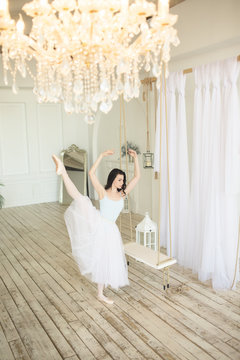 Young pretty ballerina is dancing near swing in studio with light interior
