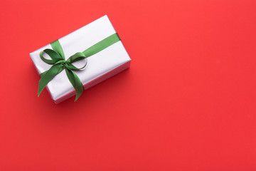 Hands holding wrapped gift box with colored ribbon as a present for Christmas, new year, mother's day, anniversary, birthday, party,  on white background, top view. Present for a colleague at work.