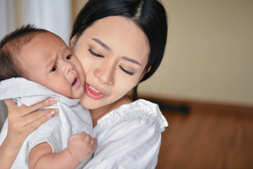 Newborn Concept. Mother and child on a white bed. Mom and baby boy playing in bedroom. Parent and little kid relaxing at home. Family having fun together. Newborn baby is fussing and crying.