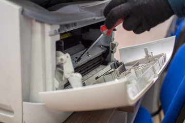 The specialist repairman serves or repairs the laser printer with a screwdriver and a brush. Servicing of copiers and printers