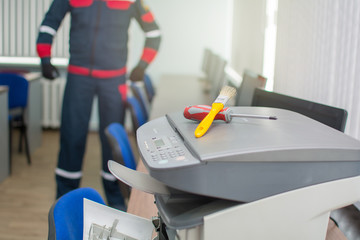 The specialist repairman serves or repairs the laser printer with a screwdriver and a brush....