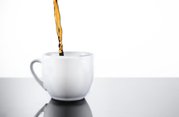 Filling a white porcelain mug cup with fresh, dark black coffee or tea
