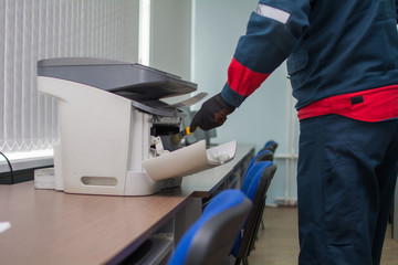 The specialist repairman serves or repairs the laser printer with a screwdriver and a brush....