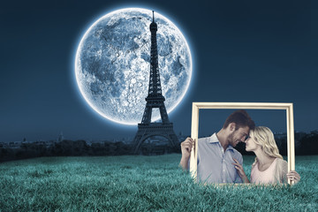 Attractive young couple holding picture frame against large moon over paris