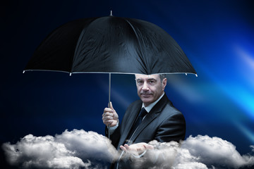 Mature businessman holding an umbrella against blue