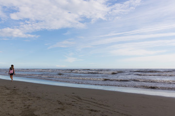 Young lady strolling on an empty beach with waves