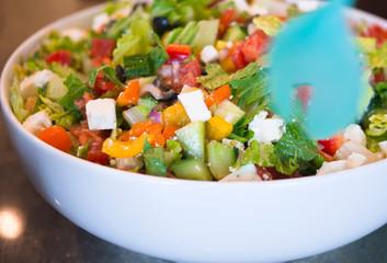 Freshly prepared salad of sliced leaves and vegetables with cheese seasoned with olive oil in a deep bowl