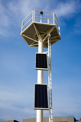 Fototapeta na wymiar beacon sky solar panels top light house transformation energy blue white sun saving beam two beach port harbor