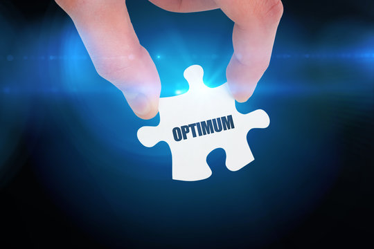 The word optimum and hand holding jigsaw piece against blue background with vignette