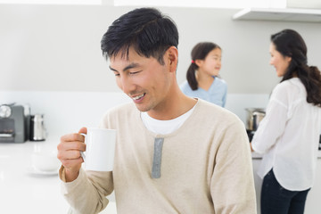 Smiling man drinking coffee with family in background