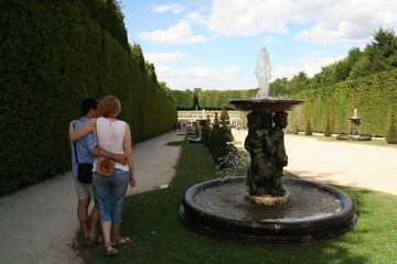 The couple of tourists observing Three Tritones statue fountain in the Versailles garden in the sunny summer day