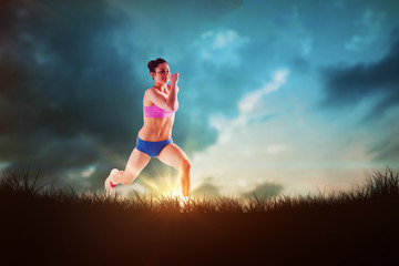 Fit brunette running and jumping against blue sky over grass