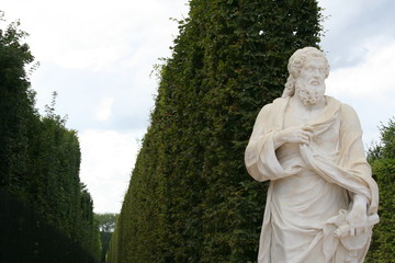 White marble statue of god in front of green fence in Versailles garden